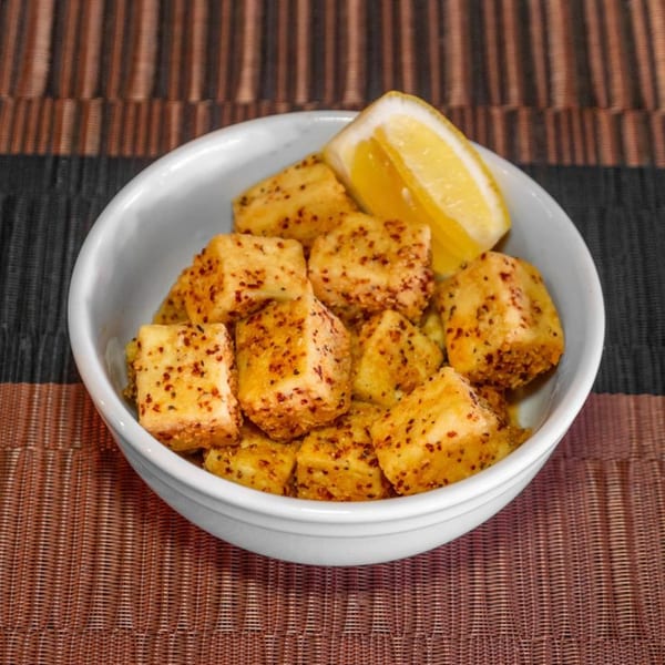 A white bowl filled with golden-brown hibachi tofu cubes, seasoned with spices, and a lemon wedge.
