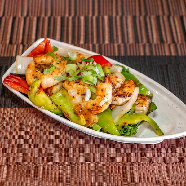 Hibachi shrimp with red and green bell peppers, onions, and scallions on a white plate.