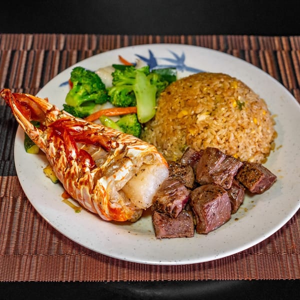 Hibachi lobster tail, steak, fried rice, and mixed vegetables on a white plate.