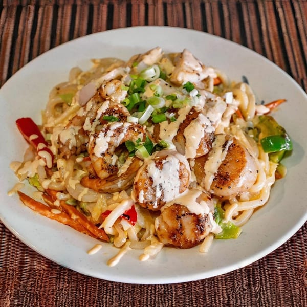 Hibachi scallops and shrimp with noodles, vegetables, and a creamy sauce, garnished with green onions.