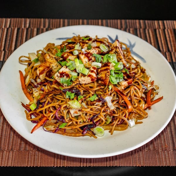 Hibachi chicken lo mein noodles with vegetables, garnished with chopped green onions and a dark sauce.